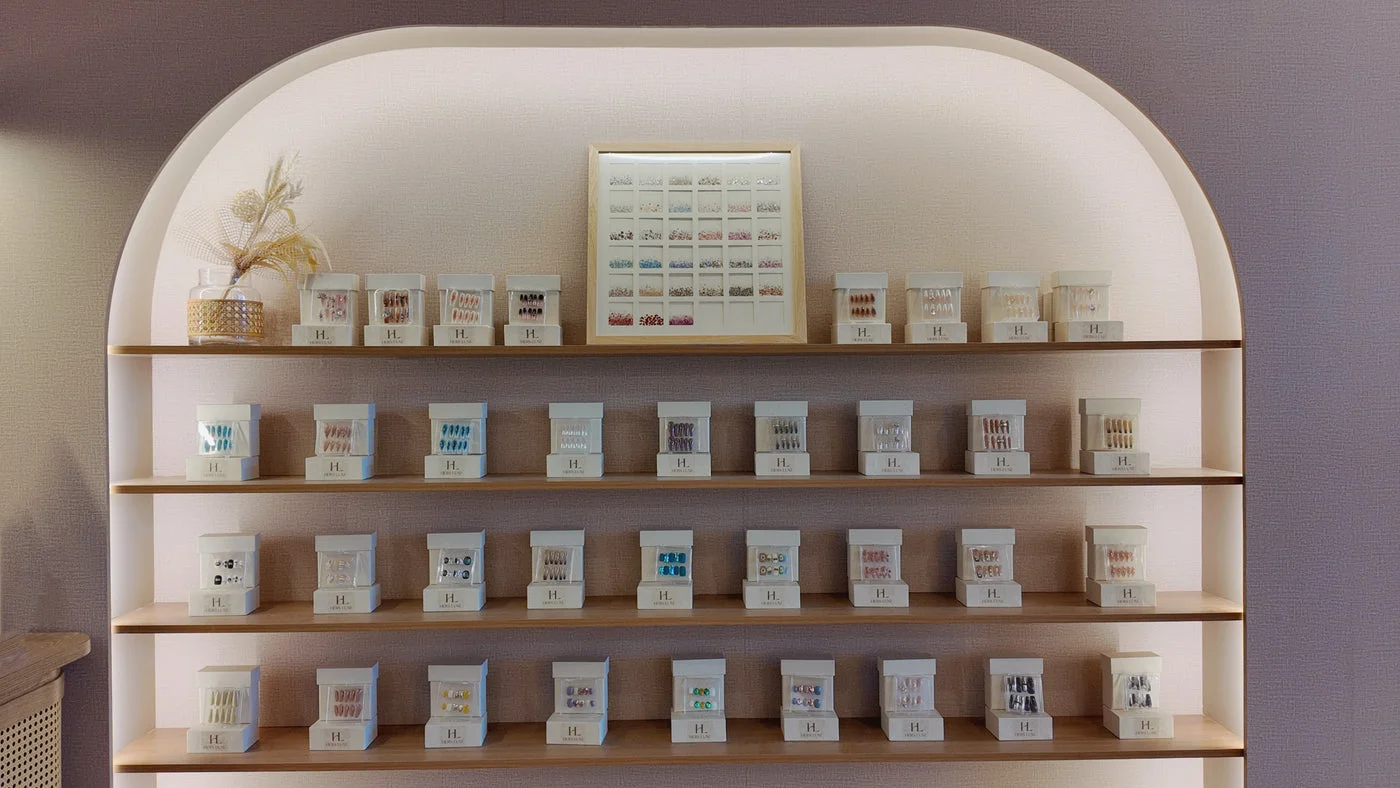 The Hers Luxe nail library — arched timber shelves of HL-branded nail sets